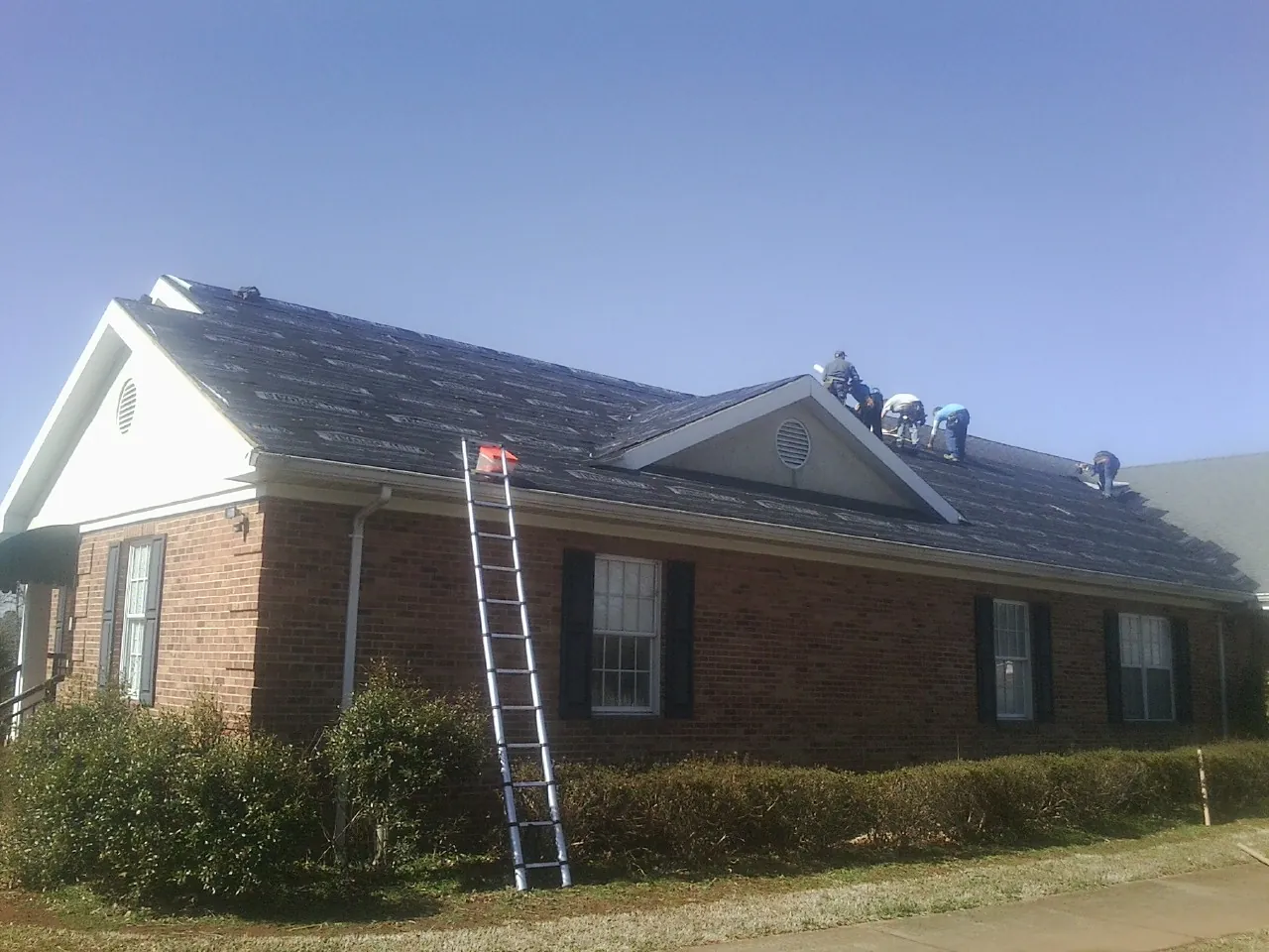 Crew tearing shingles off a brick ranch roof with a ladder set — Metal Roof Repair work by our crew in Wyckoff