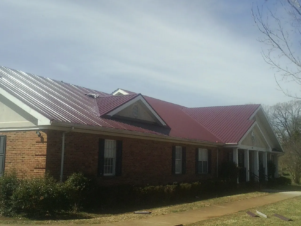 Red metal roof with gabled entries on a long brick building, from a Hail Damage Roof Repair job in Wyckoff