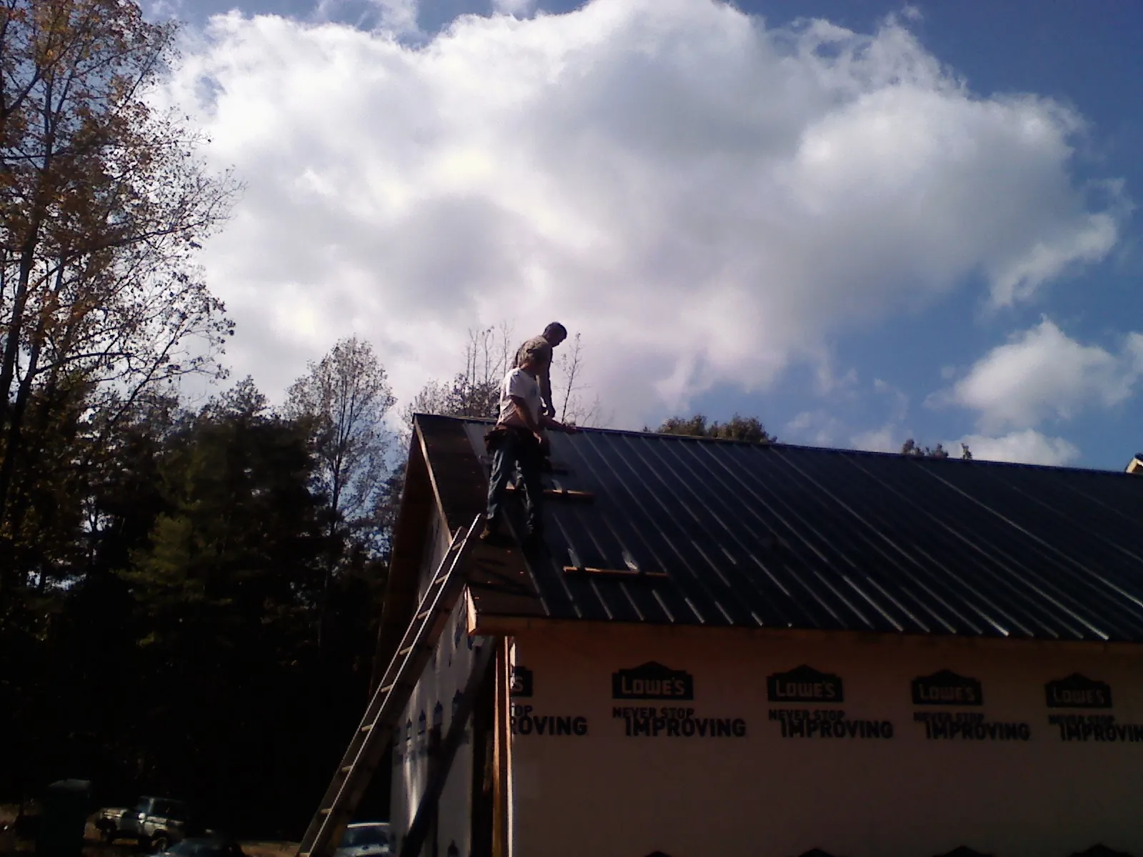 Roofer fastening dark metal panels high against a cloudy sky, from a Roof Inspection job in Wyckoff