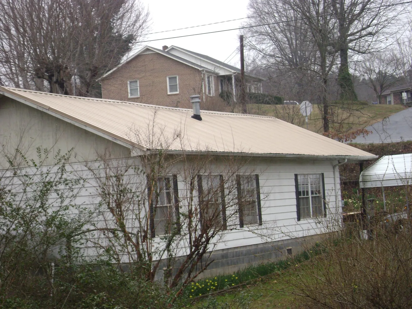 Tan metal roof on a white sided house set into a hillside — Commercial Roofing by Roofing Brothers in Wyckoff